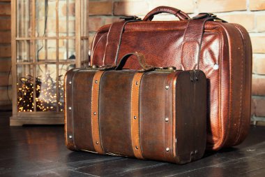 Tuğla duvara karşı ahşap katta iki kahverengi deri bavul. Retro Bagaj tasarımı. Eski bagajları ele. Seyahat ve Turizm konsepti. Gezi ve macera konsepti. Yolculuk Valise. Antika deri çanta