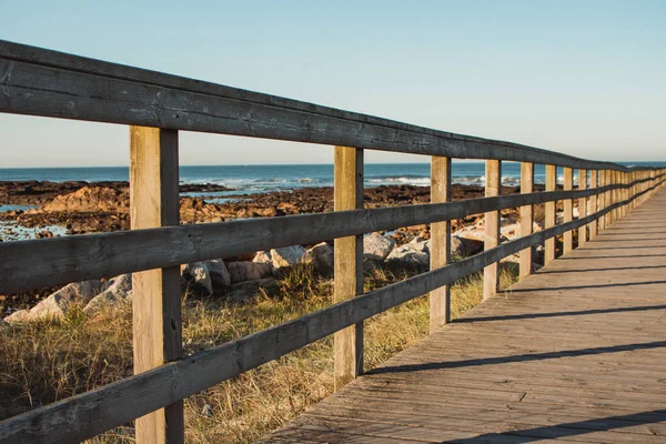 Wooden path with fence to the beach. Walkway on seashore in the morning. Travel and walk concept. Camino de Santiago landscape. Atlantic Ocean coast in Portugal. Wooden pier in perspective.