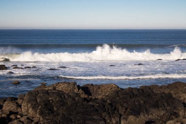 Dalgalar Atlantik Okyanusu sahilinde kayalara çarpıyor. Doğal deniz manzarası. Deniz kenarında güzel sörf. Köpük ile sıçrama dalgaları. Sahilde seyahat ve tatil. Kayalık sahil şeridi. Doğa gücü.
