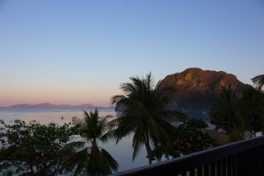 Balkondan tropikal sabah koyungüzel bir görünüm. Ağaçlar ve tekneler ile Filipinler adada Sabah. Palawan, Filipinler'de gün doğumu. Tropik adalar sabah alacakaranlıkta ağaçlarla ön planda. Asya manzarası. Yaz tatili.