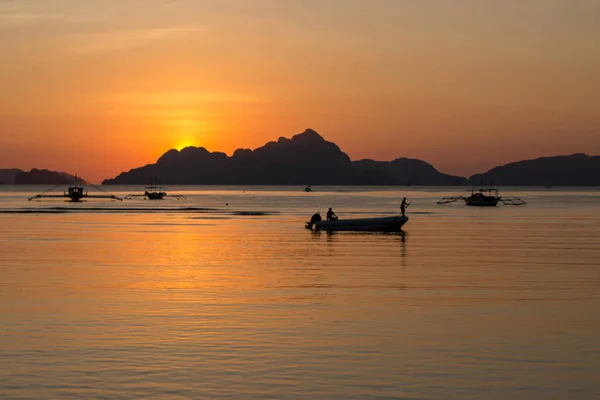 Silhouettes of boats in tropical harbor in the evening. Sunset in lagoon in Philippines, Palawan, El Nido. Sunset on beach. Scenic sunset with mountains isles on horizon. Summer vacation and travel. Exotic landscape.