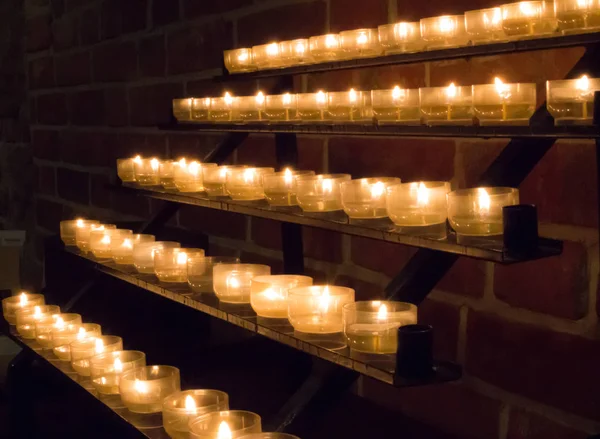 Row of glowing candles in church. Candles with flame on dark background. Faith and religion concept. Candles in catholic church. Peace and hope concept. Candlelight background. Church interior.