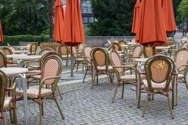 Empty outdoor cafe with closed umbrellas. Street cafe with empty tables and chairs. Restaurant furniture concept. European cafe in summer patio. Summer terrace with tables and free seats.