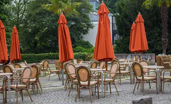 Empty outdoor cafe with closed umbrellas. Street cafe with empty tables and chairs. Restaurant furniture concept. European cafe in summer patio. Summer terrace with tables and free seats.