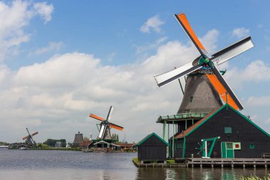 Zaanse Schans, Hollanda - 14.06.2019: Tarihi köydeki eski Hollanda yel değirmenleri. Nehir ile alanda ahşap değirmenler. Avrupa'da tarihi mimari. Kırsal Hollanda dönüm noktası. Rüzgar enerjisi kavramı. 