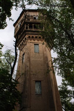 Ormanda terk edilmiş bir kule. Eski ahşap ve tuğla bina. Vintage mimari. Isınma kavramı. Ahşap balkonlu retro ev. Yıkık yüksek kulenin cephesi.