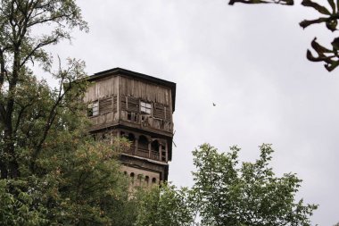 Ormanda terk edilmiş bir kule. Eski ahşap ve tuğla bina. Vintage mimari. Isınma kavramı. Ahşap balkonlu retro ev. Yıkık yüksek kulenin cephesi.