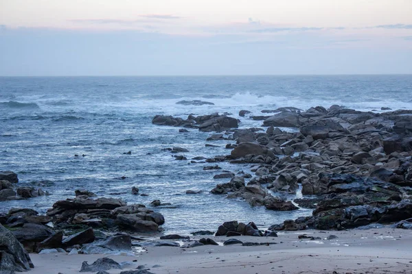 Sabah Portekiz'de Atlantik Okyanusu sahili. Mavi sabah sisinde deniz manzarası. Taşlar ve dalgalarla okyanus plajı. Boş plaj. Kayalık sahil şeridi. Sakin okyanus kıyısı. Vahşi doğa kavramı. 