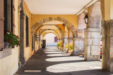 Çiçekli ve fenerli ortaçağ kemerleri. Fransa 'da boş kemer yolu. Güneşli bir günde sarı atari salonu. Antik Avrupa mimarisi. Köy binasındaki kemerli koridor yatay. Seyahat kavramı. 