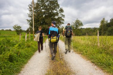 İspanya - 10 / 01 / 2019: Camino de Santiago 'da yürüyen üç bilinmeyen hacı. Köy yolunda sırt çantalı bir grup turist. Aktif insanlar yolda. Hac konsepti. Sırt çantalı adamlar. Macera ve seyahat konsepti.