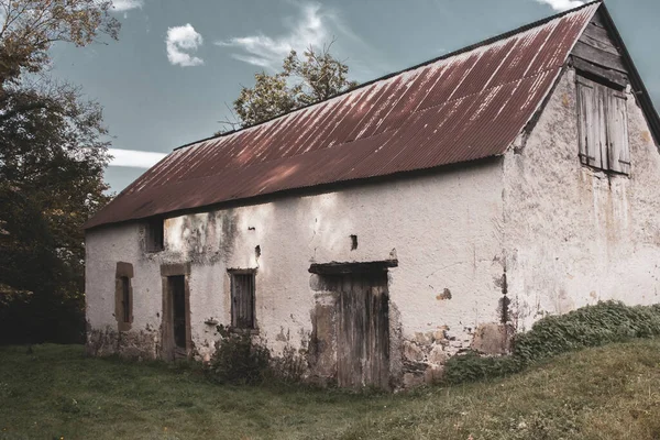 Abandoned old barn with wooden fence and grass on backyard, filtered. Weathered exterior of ancient building in village, toned image. Rural landmark. Rustic architecture in France. Scary empty house. Countryside landscape.