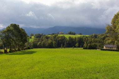 Dağlarda yaz manzarası. Dağlarda güzel bir çim ve ev. Kırsal alan. Güneşli tarlalar ve bulutlu dağlar. Pasture ve köy. Manzara vadisi. Tepelerdeki çiftlik..