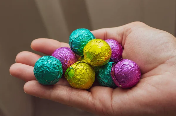 Ellerinde renkli şekerler, üst manzara. Ellerinde çikolatalı paskalya yumurtası. Paskalya sembolü. Tatlı yemek konsepti. Parlak folyoda el ele tutuşan bir grup şeker. Şenlikli yemek.. 