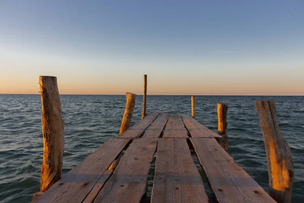 Wooden pier at the sunset. Evening sky over sea with footbridge. Calm evening landscape. Empty pier at seaside with copy scape. Pier in warm sunset light. Horizon over sea. Marine travel. Vastness concept.