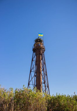 Üzerinde Ukrayna bayrağı olan eski çelik deniz feneri. Adada terk edilmiş deniz feneri, Ukrayna. Vatanseverlik kavramı. Denizci navigasyonu. Denizcilik konsepti. Ukrayna 'da yaz turizmi. Donanma navigasyonu.