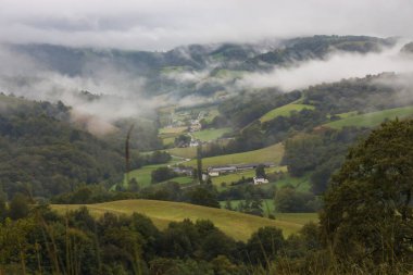 Manzaralı dağlarda sis. Köyle vadide bulutlu bir gün. Dağlarda sonbahar havası. Tepeleri, ormanı ve tarlası olan puslu bir manzara. Pyrenees dağlarının panoramik manzarası, Fransa. 