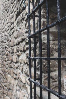 Taş duvardaki ortaçağ parmaklıkları, perspektif. Eski hapishane görüntüsü. Eski hapishanede demir ızgaralı pencere. Ceza ve ceza kavramı. Antik binada antika barlar. 