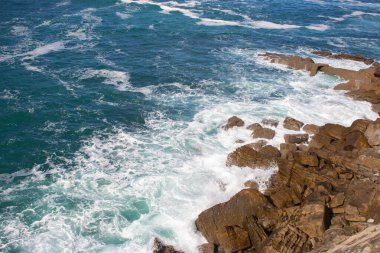 Dalgalar kayalara çarpıyor, Atlantik Okyanusu. Beyaz köpüklü gök mavisi deniz dalgaları kıyıda kırılıyor. Bir tutam akuamarin deniz suyu. Manzaralı sıçrama dalgaları. İnanılmaz bir deniz manzarası. Su hareket halinde. Deniz duvar kağıdı.