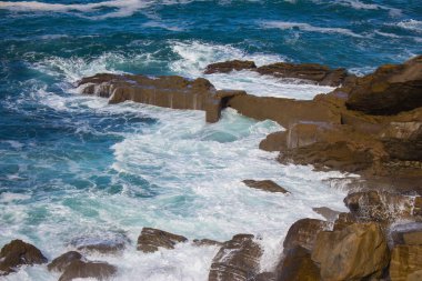 Dalgalar kayalara çarpıyor, Atlantik Okyanusu. Beyaz köpüklü gök mavisi deniz dalgaları kıyıda kırılıyor. Bir tutam akuamarin deniz suyu. Manzaralı sıçrama dalgaları. İnanılmaz bir deniz manzarası. Su hareket halinde. Deniz duvar kağıdı.