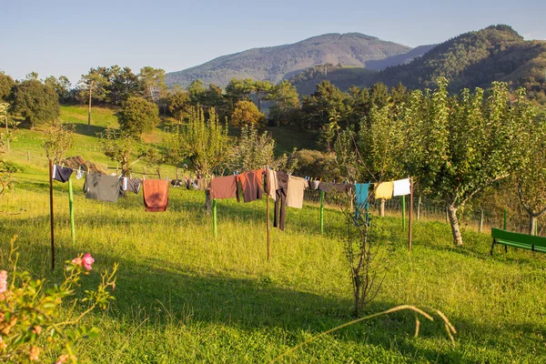 Colorful clothes on rope in garden. Wet clothes on fresh air in the village. Housework concept. Outdoor laundry. Backyard on idyllic sunny day on mountain background. Homework concept.