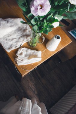 Masada beyaz örgü ve taze çiçekler. Tahta masada buketli beyaz pamuk örülmüş süveter. Örgü iğneleri ve çiçeklerle örgü işi. Ev hayatı konsepti. Samimi ev hala hayat.. 