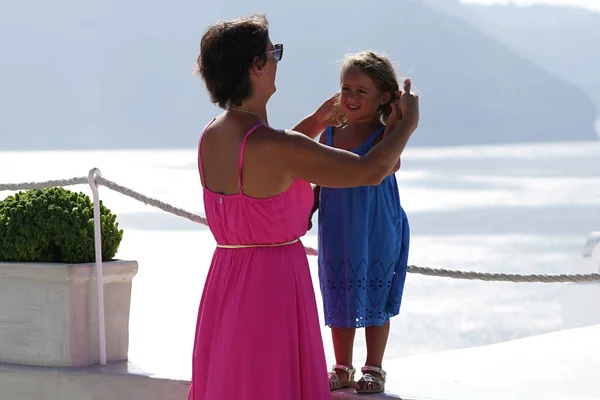 Woman with fuchsia dress plays with her little daughter on Oia Scenery as a background in Santorini, Greece