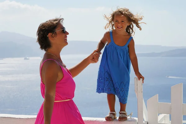 The woman in the fuchsia dress plays with a 3-4 years old girl, with the Oia Caldera Scenery as a background in Santorini, Greece