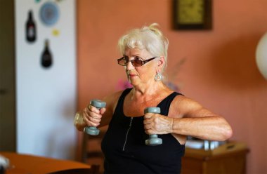 Yaşlı kadın halterlerle egzersiz yapıyor.