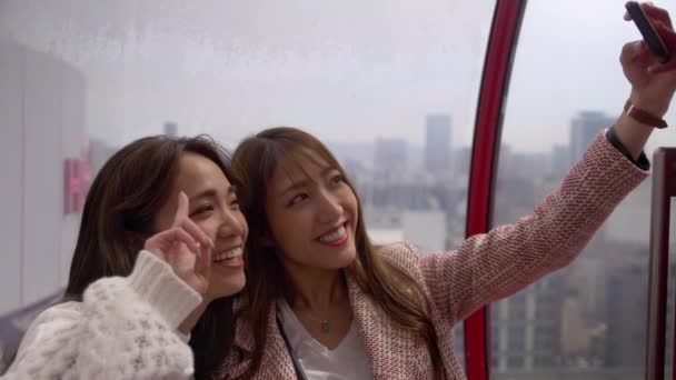Selfies を取って大きな赤い観覧車に乗っている2人の美しい友人 — ストック動画