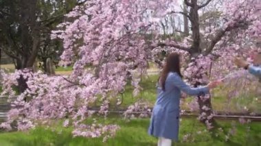 Sevimli Japon kadın Cherry Blossom parkta kabarcıklar yakalamak için çalışıyor, 4k