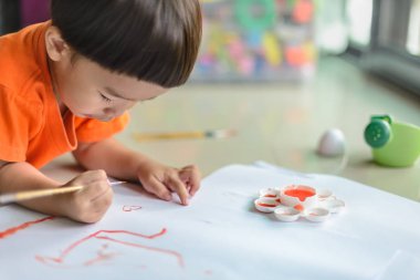 Anaokulu çocukları turuncu gömlek giyer. Turuncu kalp şeklinde boya fırçası kullanırlar..