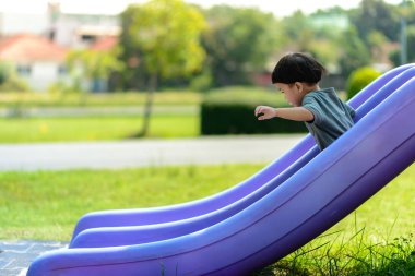 Asyalı çocuk parkta sürgülü oynuyor. Ev dışında iyi bir deneyim yaratma faaliyetleri.