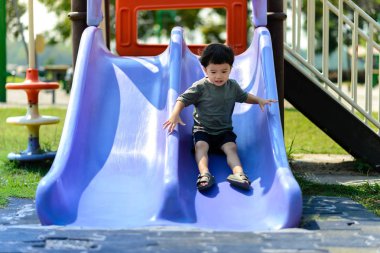 Asyalı çocuk parkta sürgülü oynuyor. Ev dışında iyi bir deneyim yaratma faaliyetleri.