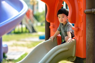 Asyalı çocuk parkta sürgülü oynuyor. Ev dışında iyi bir deneyim yaratma faaliyetleri.