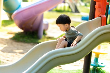 Asyalı çocuk parkta sürgülü oynuyor. Ev dışında iyi bir deneyim yaratma faaliyetleri.