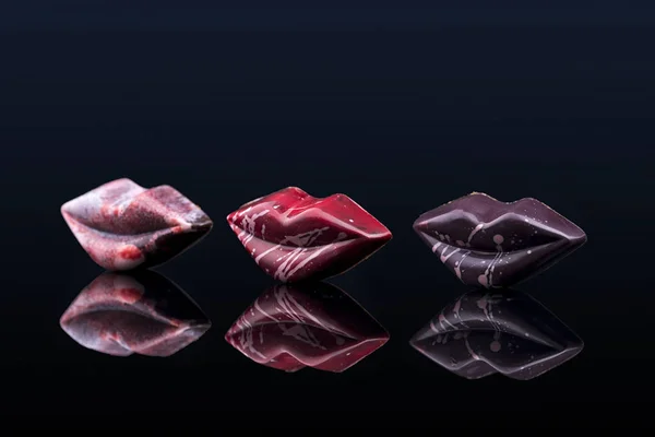 colorful chocolate candies in shape of lips with filling on black background with reflection