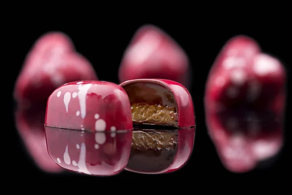 Chocolate candies with bright pink glaze on black background with reflection