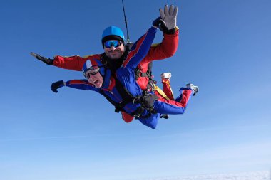 Tandem skydiving. Büyük adam ve bir kadın birlikte gökyüzünde uçuyor.