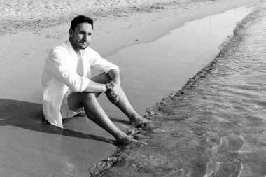 Yakışıklı adam beyaz gömlek daimi bir plajda yaz günü hayattan zevk sıcak bakıyor. Vahşi erkek model su çıplak Göğüs dışarı, sırıtma üzerinde görünüm ve tarz gözleri ile gülümseyen ıslak kısa ile poz veriyor. Tatilde yalnız ve üzgün üzgün yüz adam