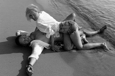 Islak gömlek gülümseyen seviyorum bir beyaz kum plajda yatan aşık güzel mutlu çift. Su ıslak giysileri öpüşme ve gülüyor ve deniz seyir eğleniyor seksi güzel sarışın kadın ve yakışıklı sakallı erkek