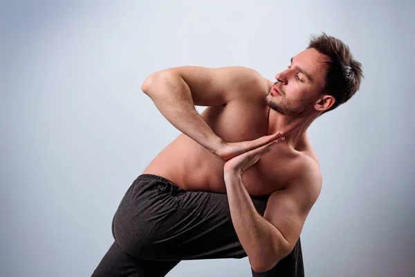 Calm peaceful young bearded Caucasian yoga instructor posing shirtless and barefooted in white studio, stretching. Attractie man practicing advanced yoga. A series of poses. Guy doing lunge exercise.