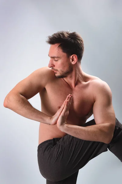 Calm peaceful young bearded Caucasian yoga instructor posing shirtless and barefooted in white studio, stretching. Attractie man practicing advanced yoga. A series of poses. Guy doing lunge exercise.