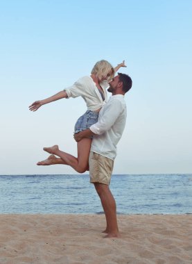 güzel çift hawaii tatil plaj manzarası arıyorum onların tadını seviyorum. Sevimli sarışın kadın ve sakallı yakışıklı bir kum sarılma üzerinde ayakta, el ele tutuşarak, deniz tarafında izlerken beyaz gömlek içinde.