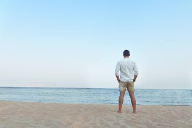 Yakışıklı adam beyaz gömlek daimi bir plajda yaz günü hayattan zevk sıcak bakıyor. Vahşi erkek model su çıplak Göğüs dışarı, sırıtma üzerinde görünüm ve tarz gözleri ile gülümseyen ıslak kısa ile poz veriyor.