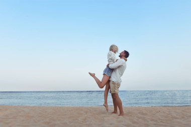 güzel çift hawaii tatil plaj manzarası arıyorum onların tadını seviyorum. Sevimli sarışın kadın ve sakallı yakışıklı bir kum sarılma üzerinde ayakta, el ele tutuşarak, deniz tarafında izlerken beyaz gömlek içinde.