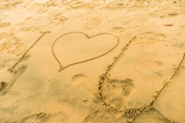 Kum kıyısındaki ilham verici işaretler, mesajlar, resimler. Ayaklar kalbe ok ile yakın dursun. Yaz tatili kumsalı Sevgililer Günü 'nde seyahat etmek için ilham verir. Aşk çiftleri ya da aile tatilleri için romantik bir seyahat. Rahatlatıcı işaret Sarı kumlarda seni seviyorum.