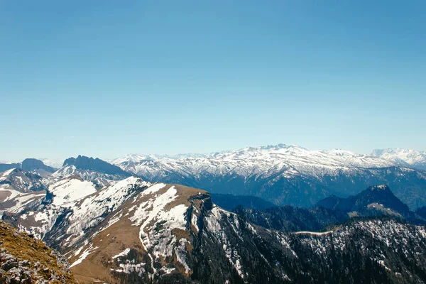 A mountain range with thawing snow and ice in the spring, against the background of forest slopes under a blue sky in the clouds.