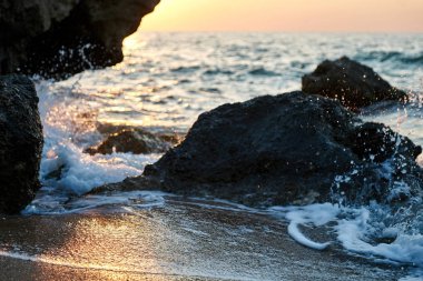 Splash dalgalar güzel gün batımı ve gökyüzü ile kayalara çarptı                               