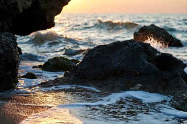 Splash dalgalar güzel gün batımı ve gökyüzü ile kayalara çarptı                               