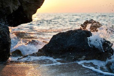 Günbatımı deniz kenarında. Altın kumlar. Dalgalar deniz kumları ve kayalar üzerinde rulo.                               